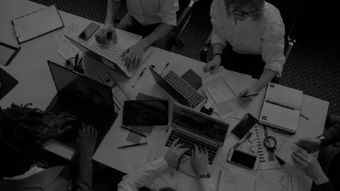 Small group of workers collaborating around a table with charts, laptops and other devices.
